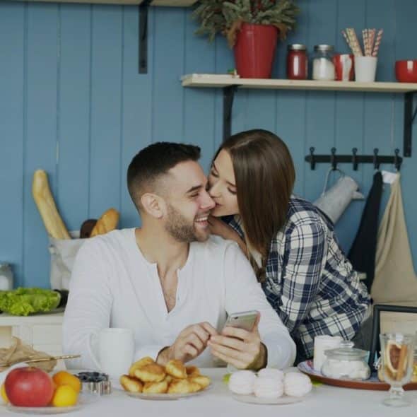 A woman kissing her husband in the kitchen