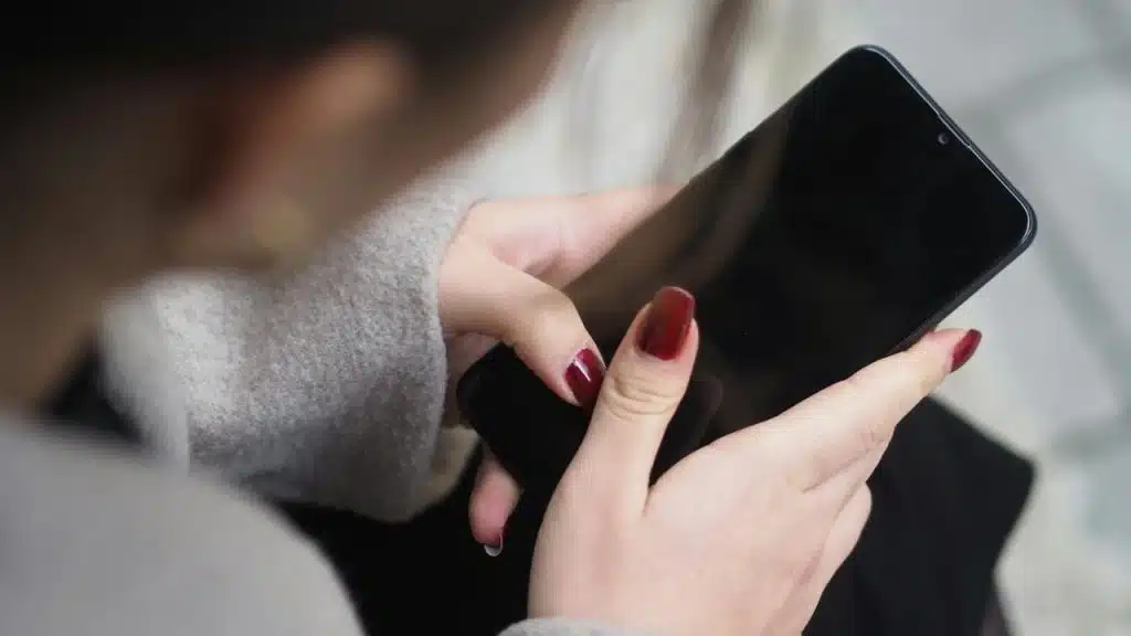 A close-up of a woman’s hands with red nails holding a smartphone.