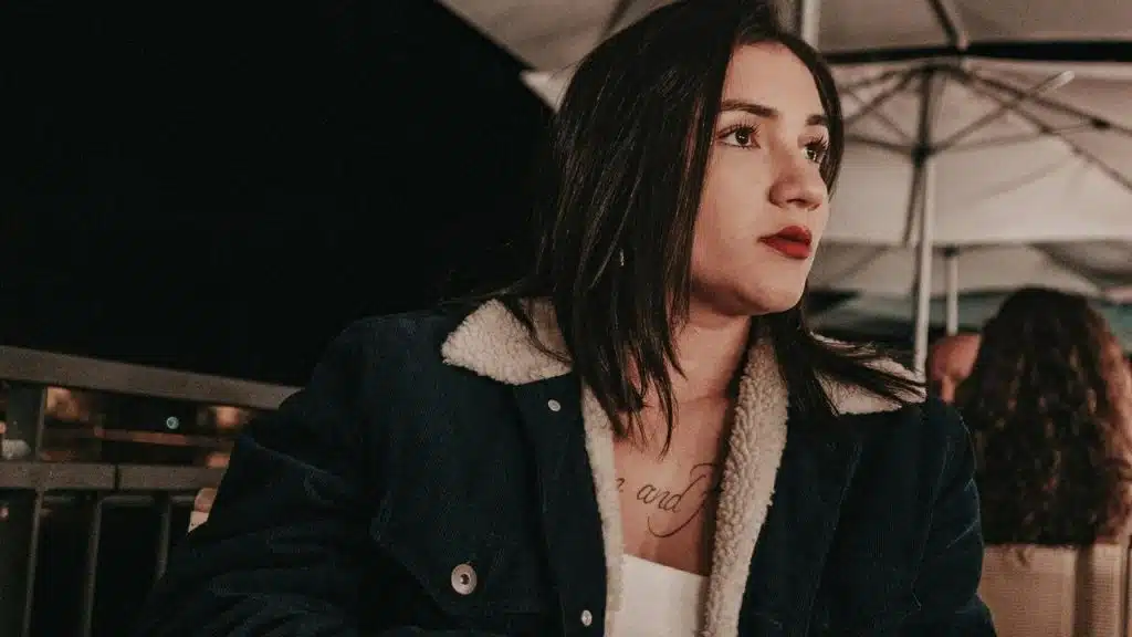 A woman sitting outdoors at night, looking off to the side with a thoughtful expression.