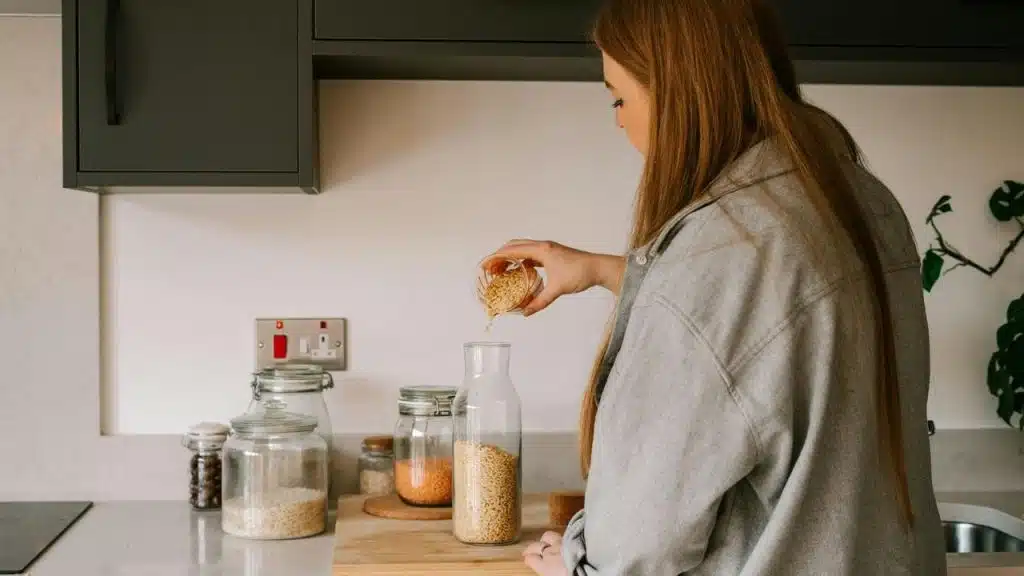 A woman pouring dry pasta into a glass jar in the kitchen.