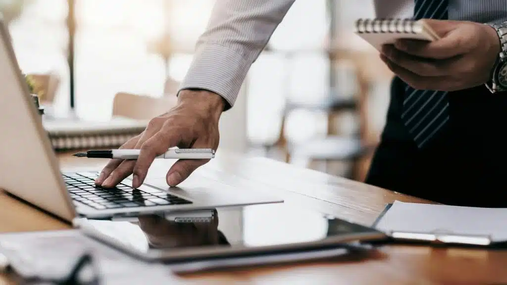 A person working at a desk with a laptop, notebook, and pen.