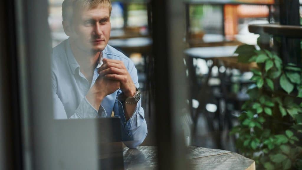 A person sitting at a table and looking out a window thoughtfully.