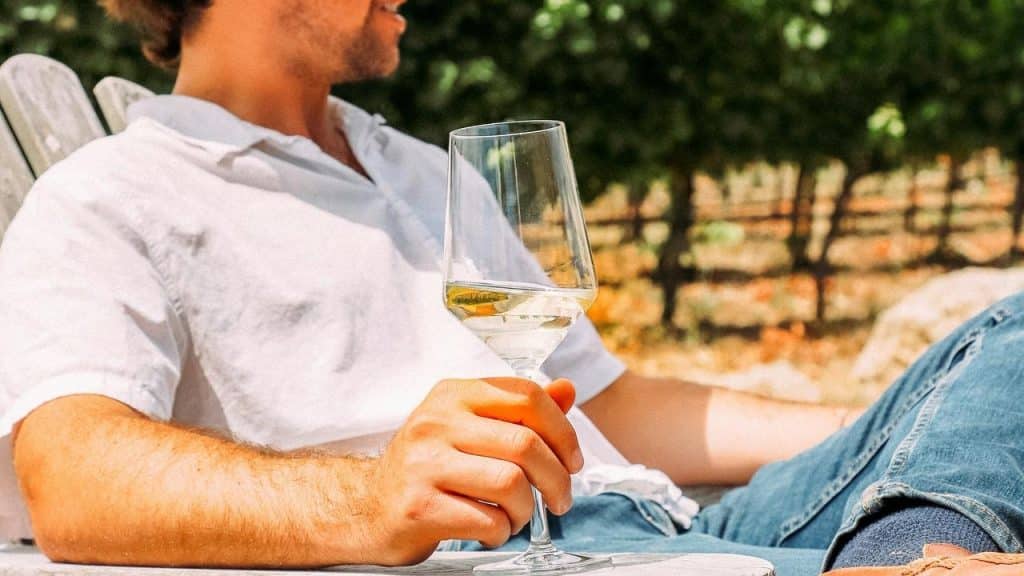 A person relaxing outdoors in a chair while holding a glass of white wine.