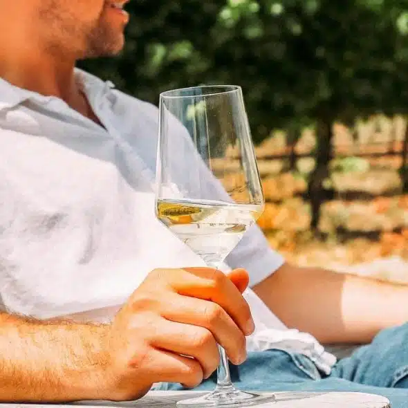 A person relaxing outdoors in a chair while holding a glass of white wine.