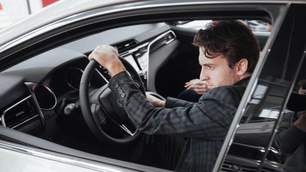 A man in a checkered suit sitting in a car holding the steering wheel.