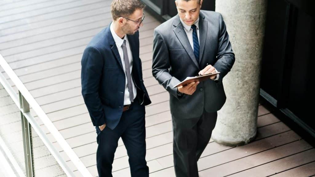 A pair of people in business suits walking and reviewing a clipboard.
