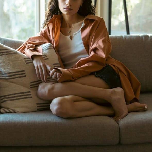 A woman sitting cross-legged on a couch near a bright window.
