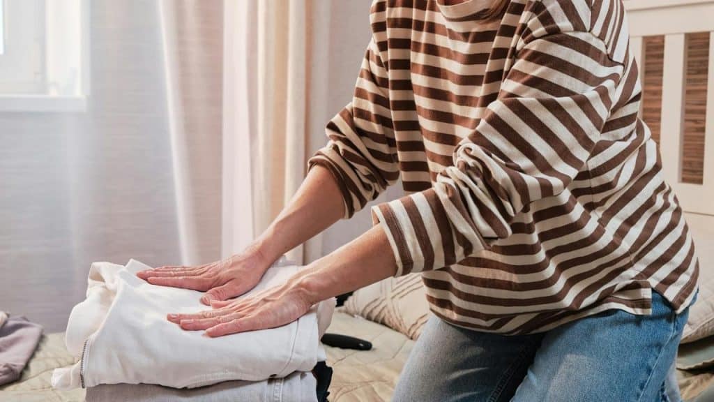 A person folds clothes on a bed.