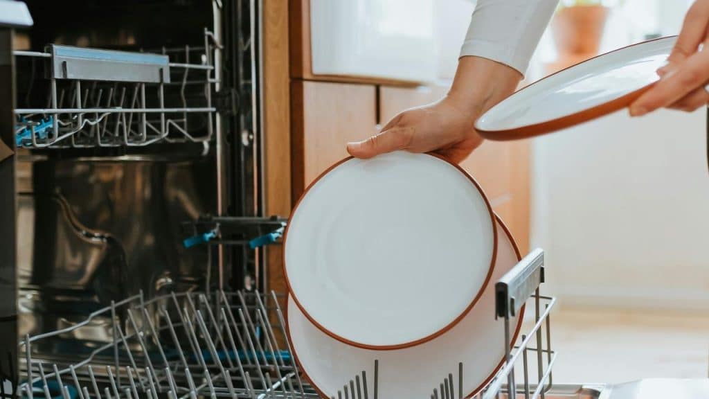 A person loading plates into a dishwasher.