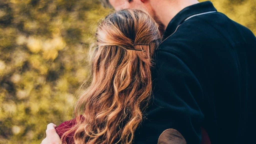A couple embracing outdoors with the woman’s head resting on the man’s shoulder.