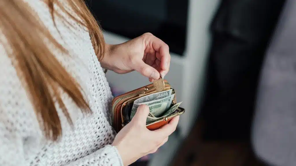 A person holding a small wallet with cash and coins.