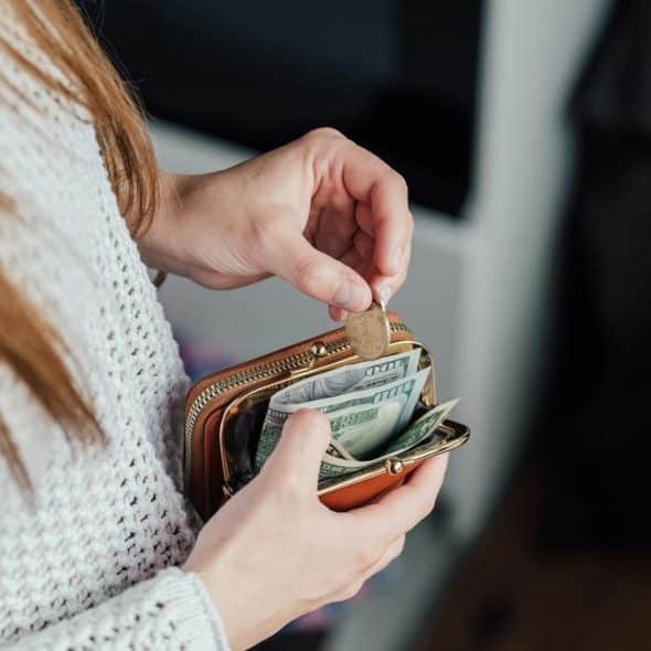 A person holding a small wallet with cash and coins.