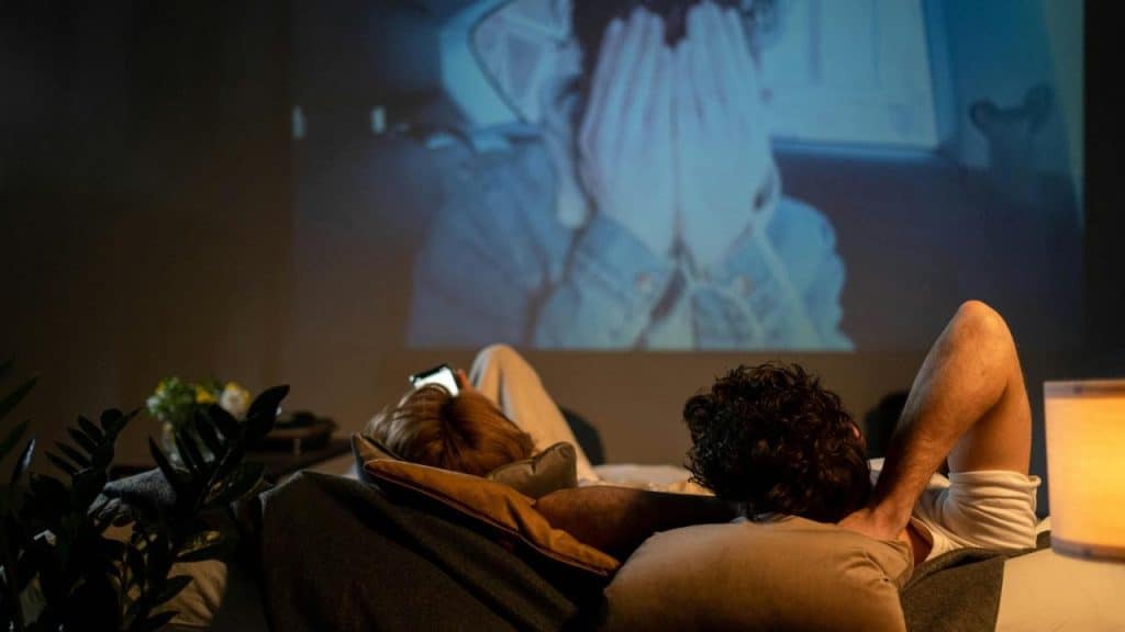 A couple lying on a bed watching a movie projected on the wall.