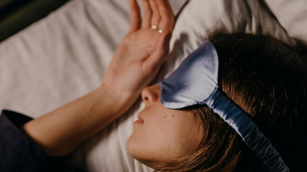 A person sleeping in bed wearing a blue sleep mask.