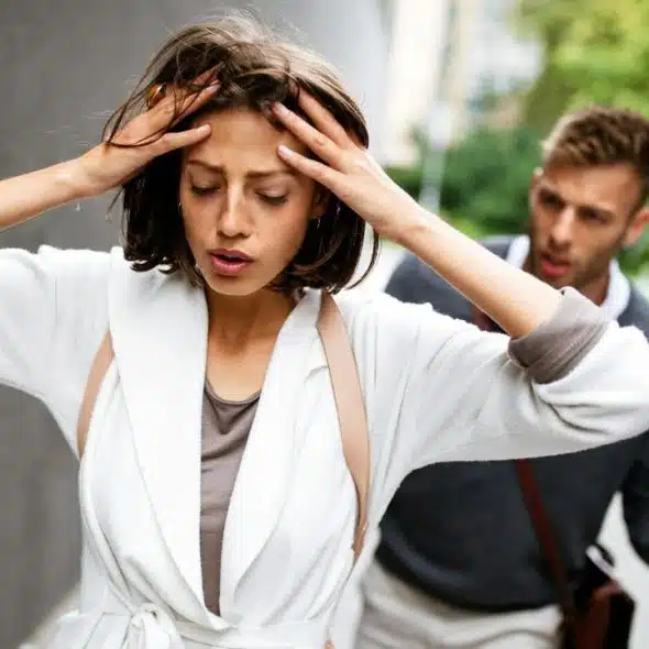 A distressed woman holds her head while a blurred man gestures behind her.