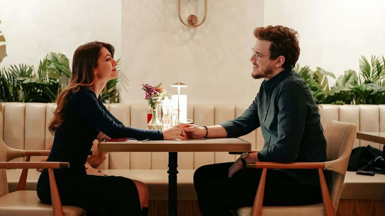 Couple holding hands across a restaurant table, looking and smiling at each other.