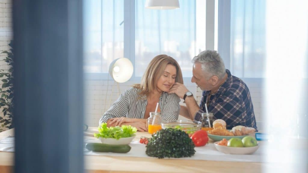 Middle-aged man caresses woman's cheek as they sit at a table full of food.