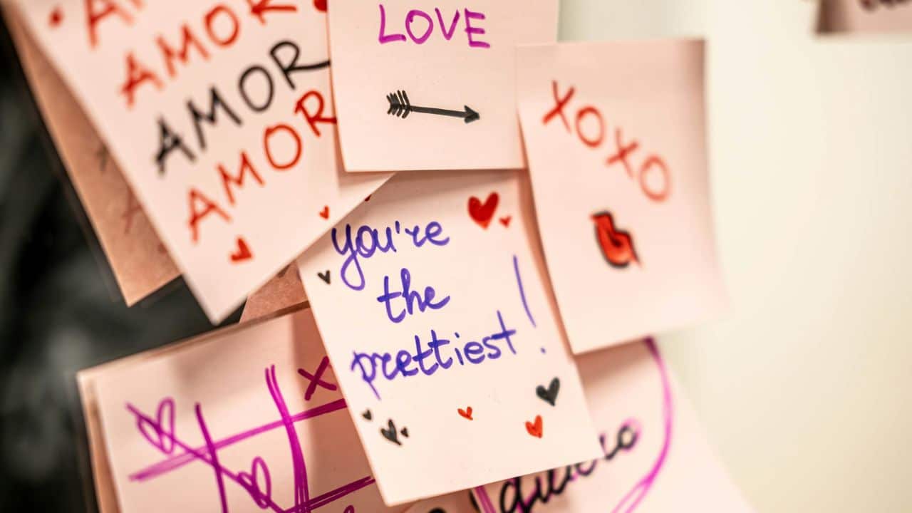 Close-up of multiple pink sticky notes with handwritten words like "LOVE," "XOXO," and "you're the prettiest!"