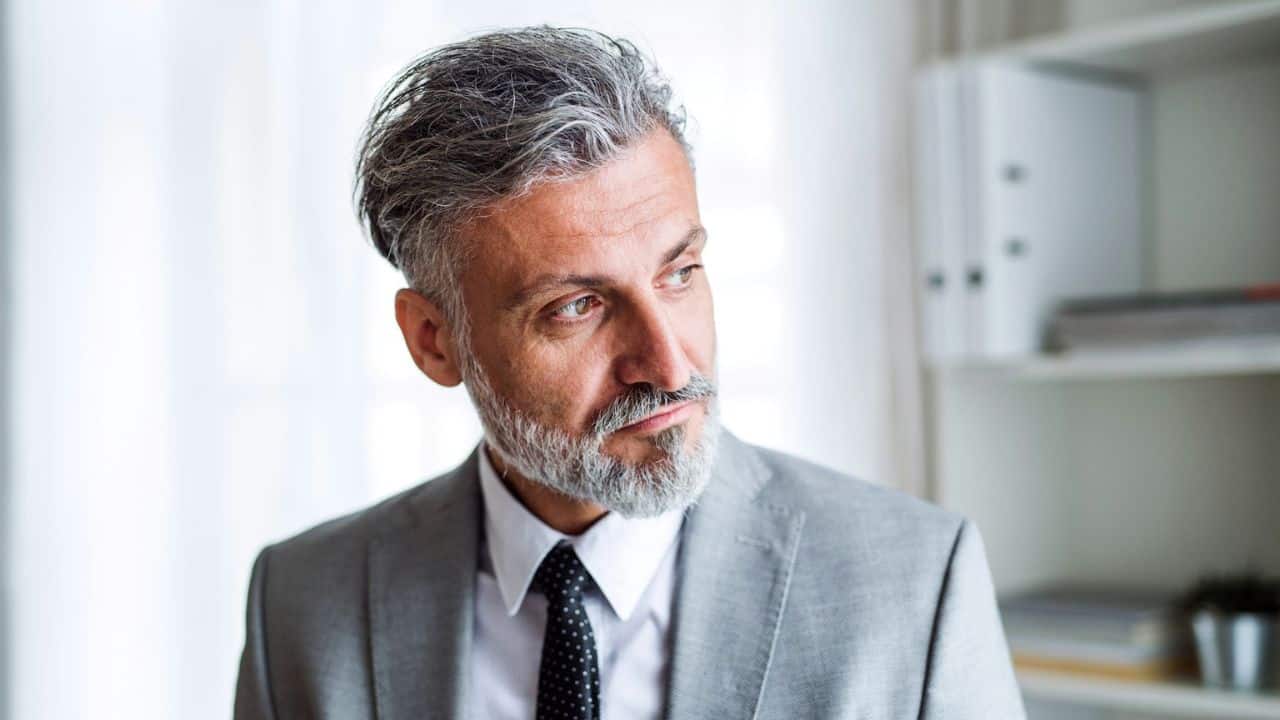 A handsome middle-aged man in a suit looks off to the side in an office.