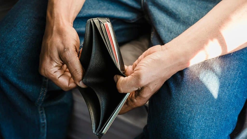 A person sitting with their legs crossed, holding an open empty wallet.
