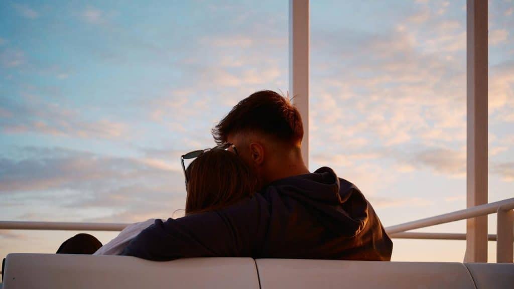 A couple sitting close together on a bench watching the sunset.