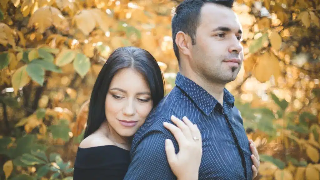 A woman hugging his husband from behind who is lost in thoughts.