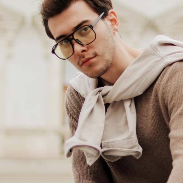 A young man in glasses and a sweater with a jacket tied over his shoulders.