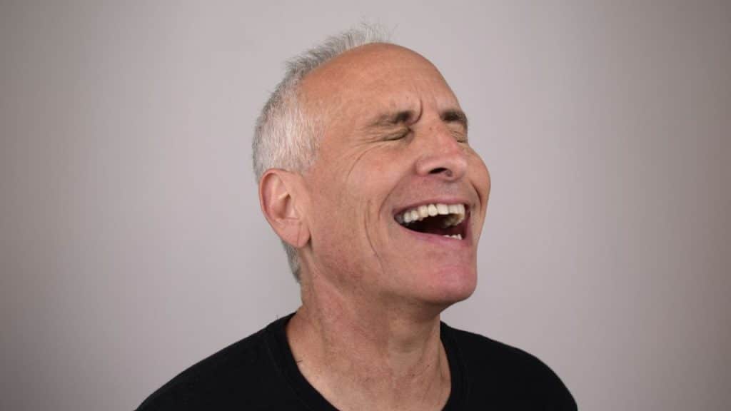 A smiling man with his eyes closed is laughing with his head tilted back.