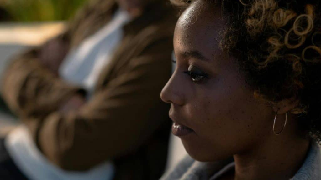 A woman with curly hair and hoop earrings looking thoughtful.