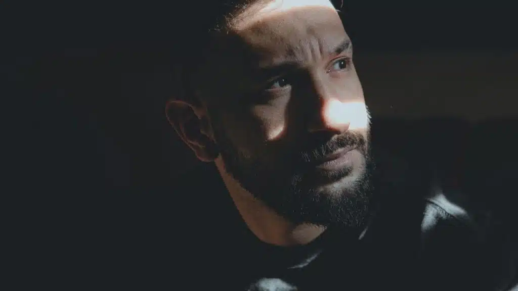 A bearded man in dramatic lighting with sunlight cast across his face.