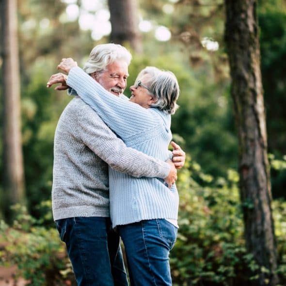 An old couple embrace each other in a forest.