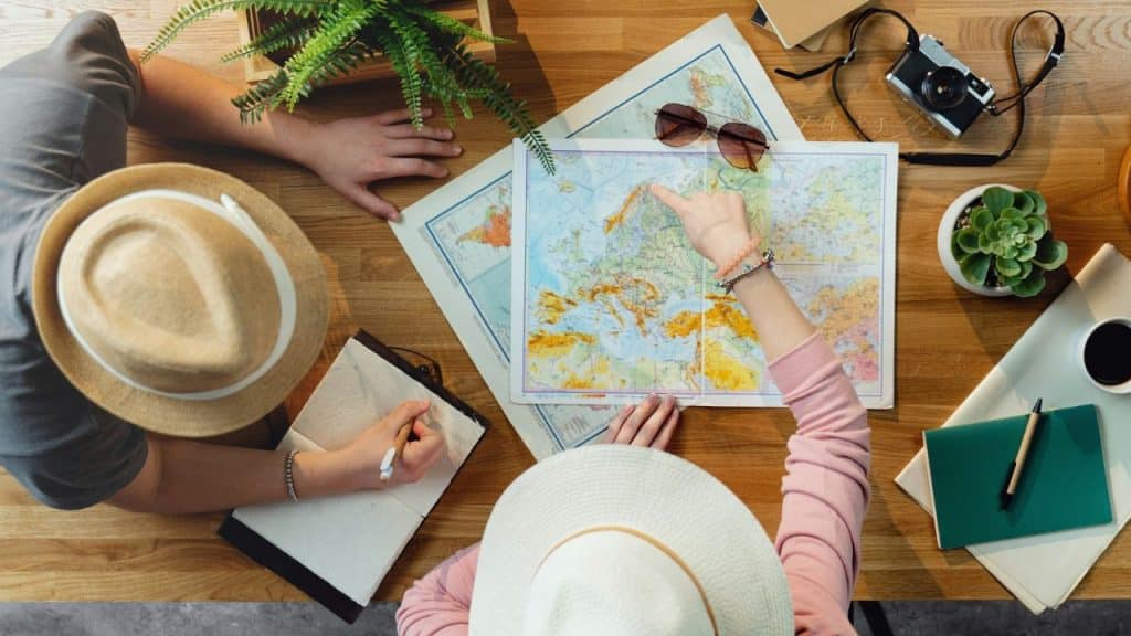 Two people wearing hats sit at a table looking at a map and pointing at a location.