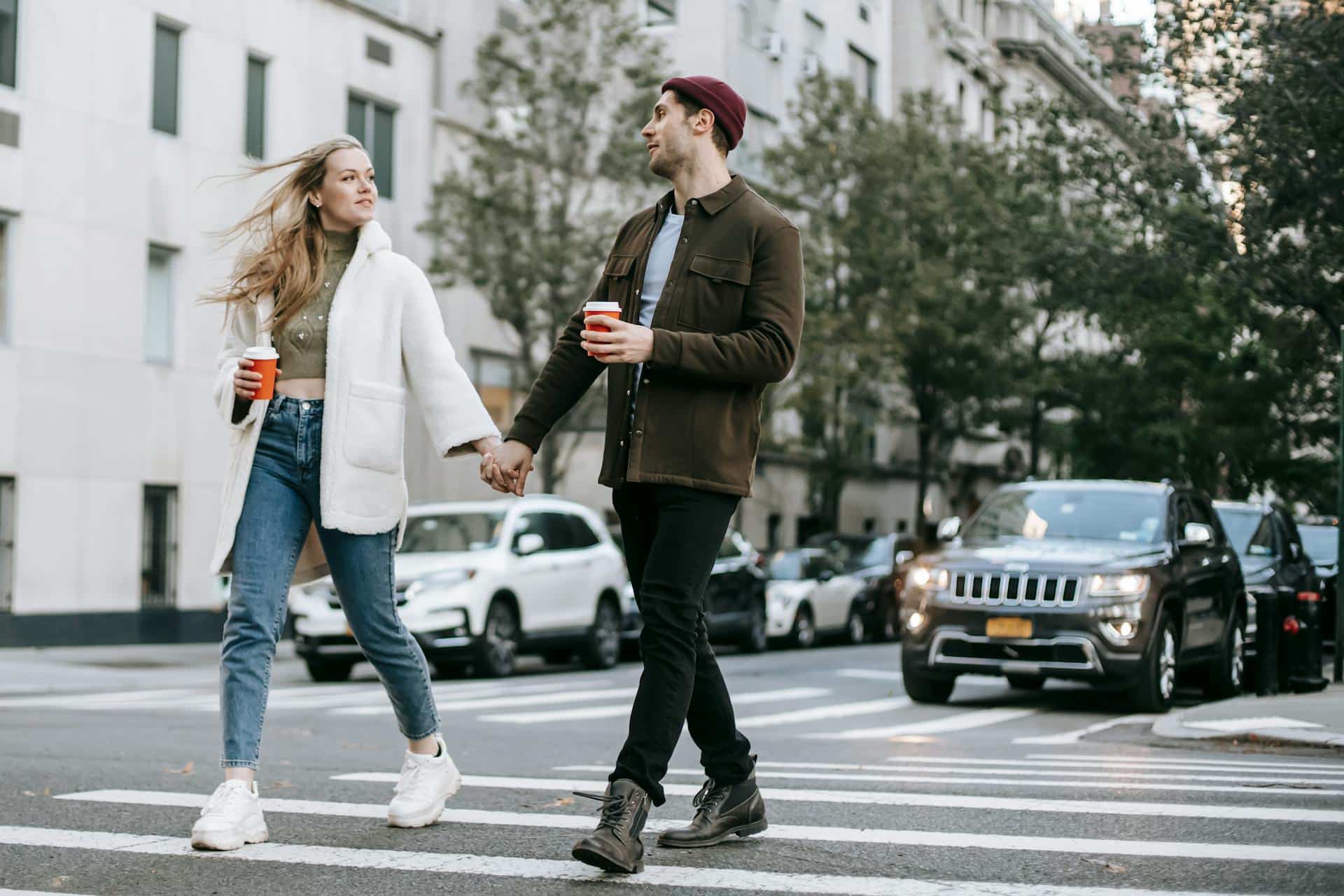 A man and a woman walking through a crosswalk while holding hands.