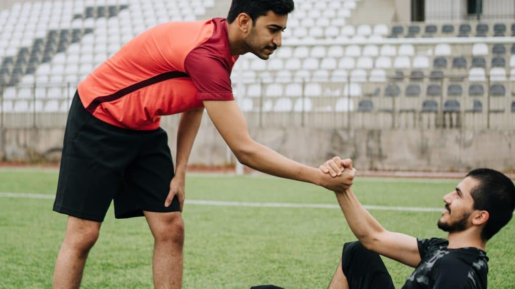 A man offering his hand to a man lying on the ground and pulling him to his feet.