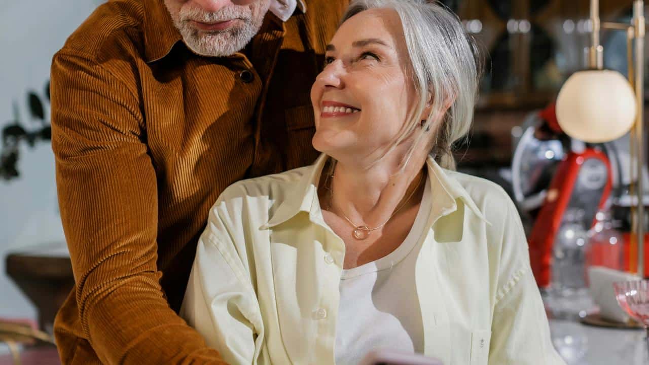 A smiling older woman looking up at her partner in a cozy indoor setting.