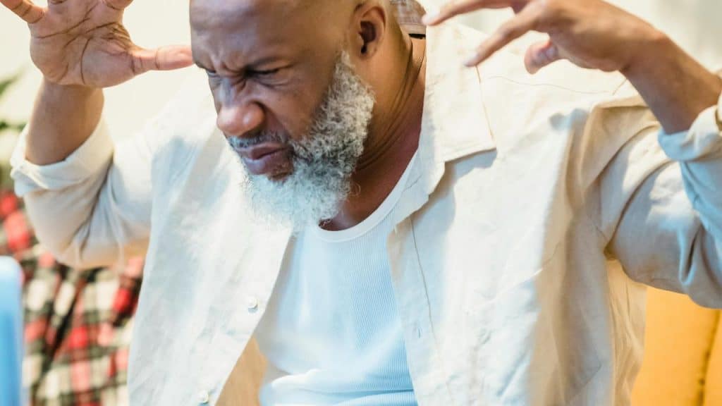 A man grimacing with his hands raised in frustration.