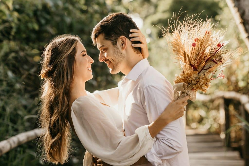 A man looking at the woman in a white dress holding a bouquet.