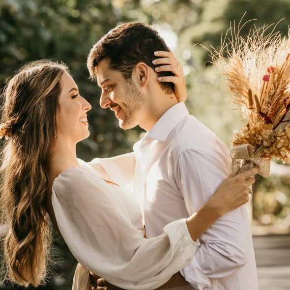 A man looking at the woman in a white dress holding a bouquet.