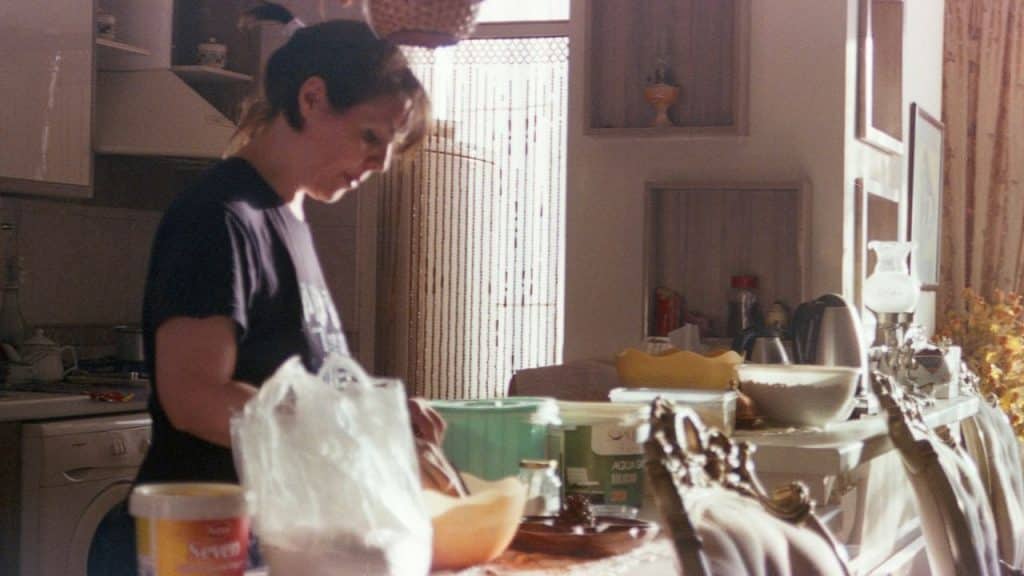 Woman in a dark shirt standing over a bowl on a messy kitchen counter.