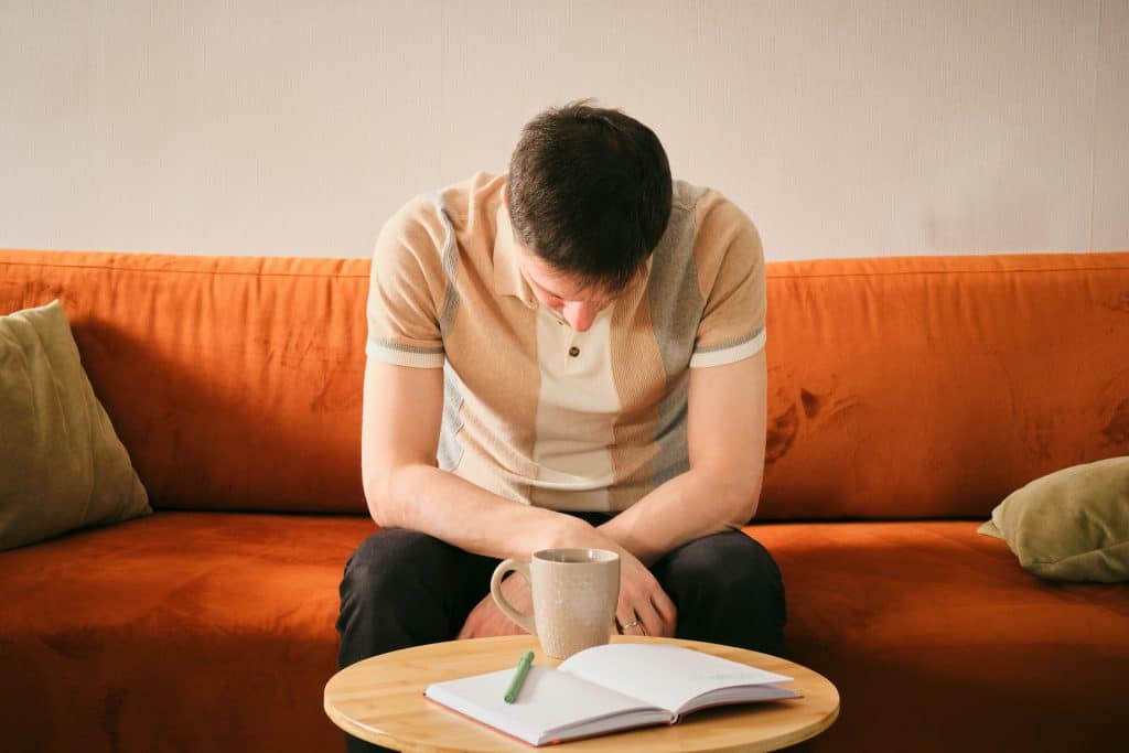 A man sitting on an orange couch, looking down.