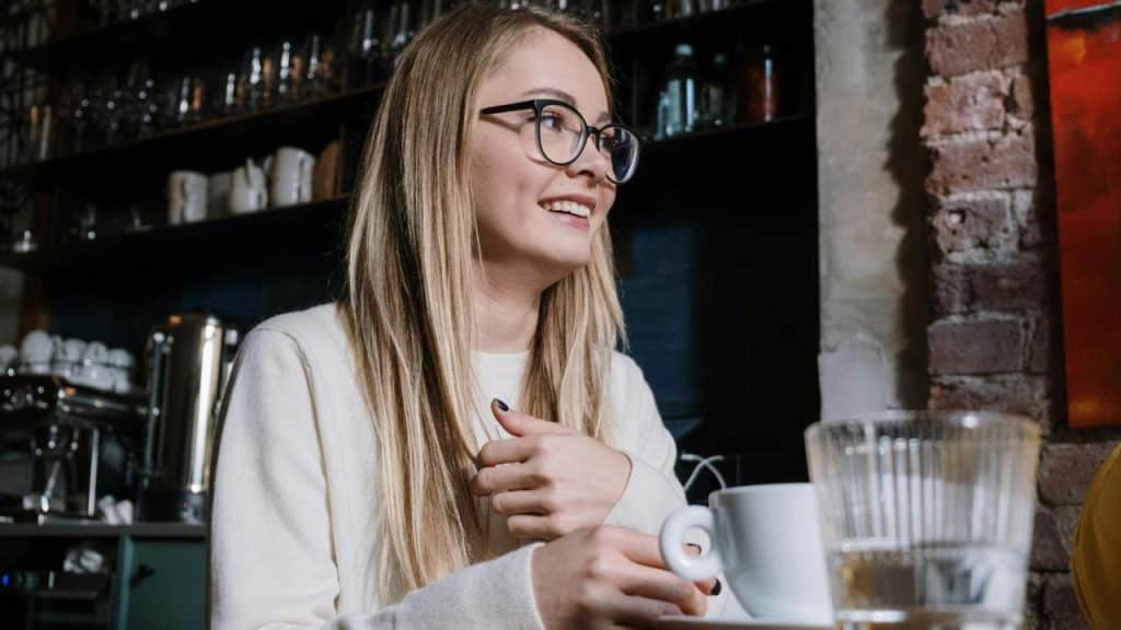 A woman smiling while holding a coffee cup in a café.