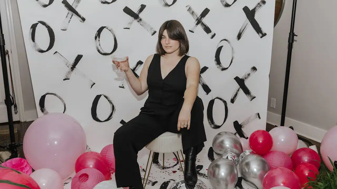 A woman is sitting on a chair surrounded by balloons.