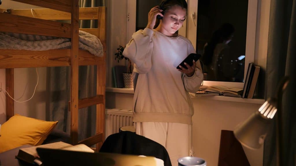 A person wearing headphones and looking at a phone in a bedroom.