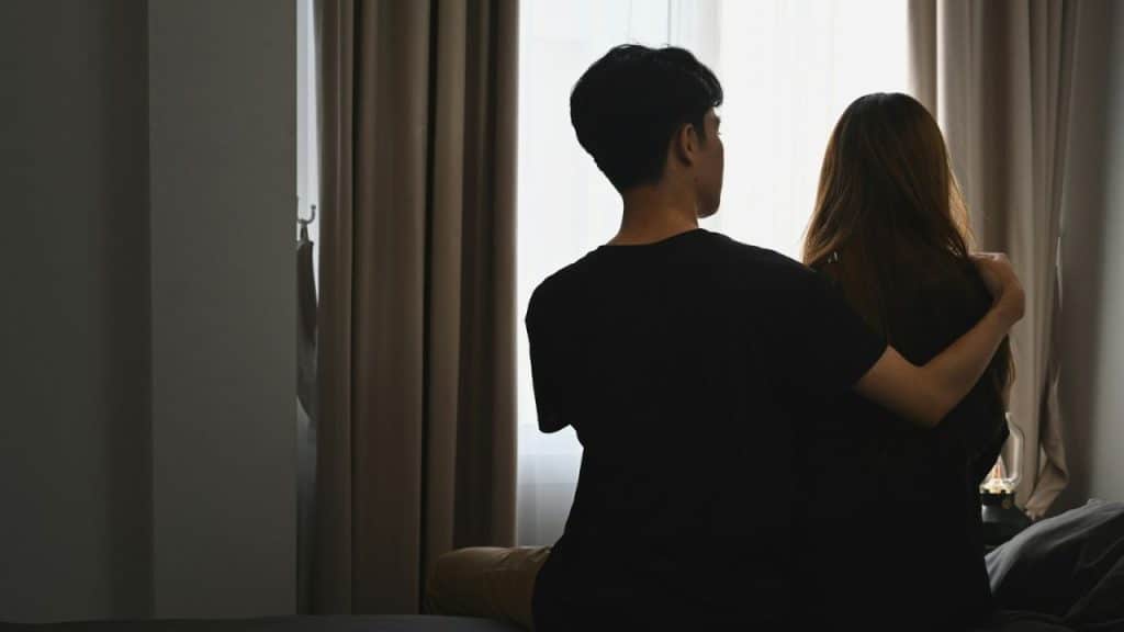 Rear view of a couple sitting close together, looking out a bright window.