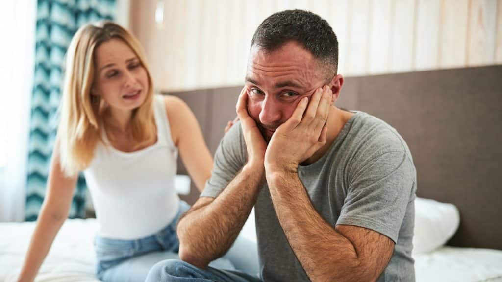 A handsome man holding his face with his hands and looking at the camera while a woman touches his shoulder.