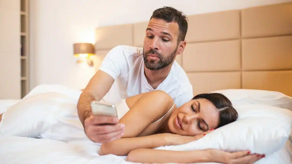 Man checking the phone of a woman who is sleeping beside him.