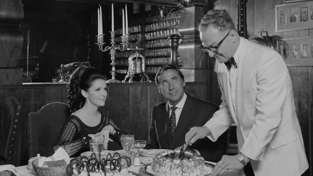 A black-and-white photo of a man cutting a cake.