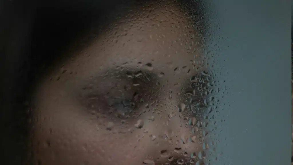 A woman behind a glass window with moisture.