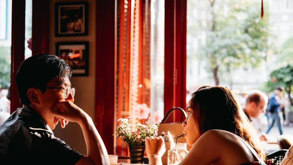 A man wearing glasses looking at a woman sipping on a straw.