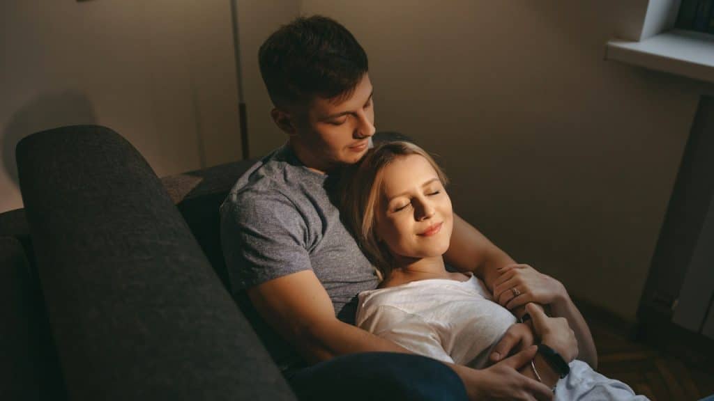 A lovely Caucasian woman with blonde hair lying on her lover on a sofa and embracing together.